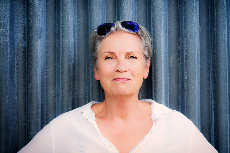 Portrait von fraujahnke mit Sonnenbrille in den Haaren vor samtig-blauem Vorhang.